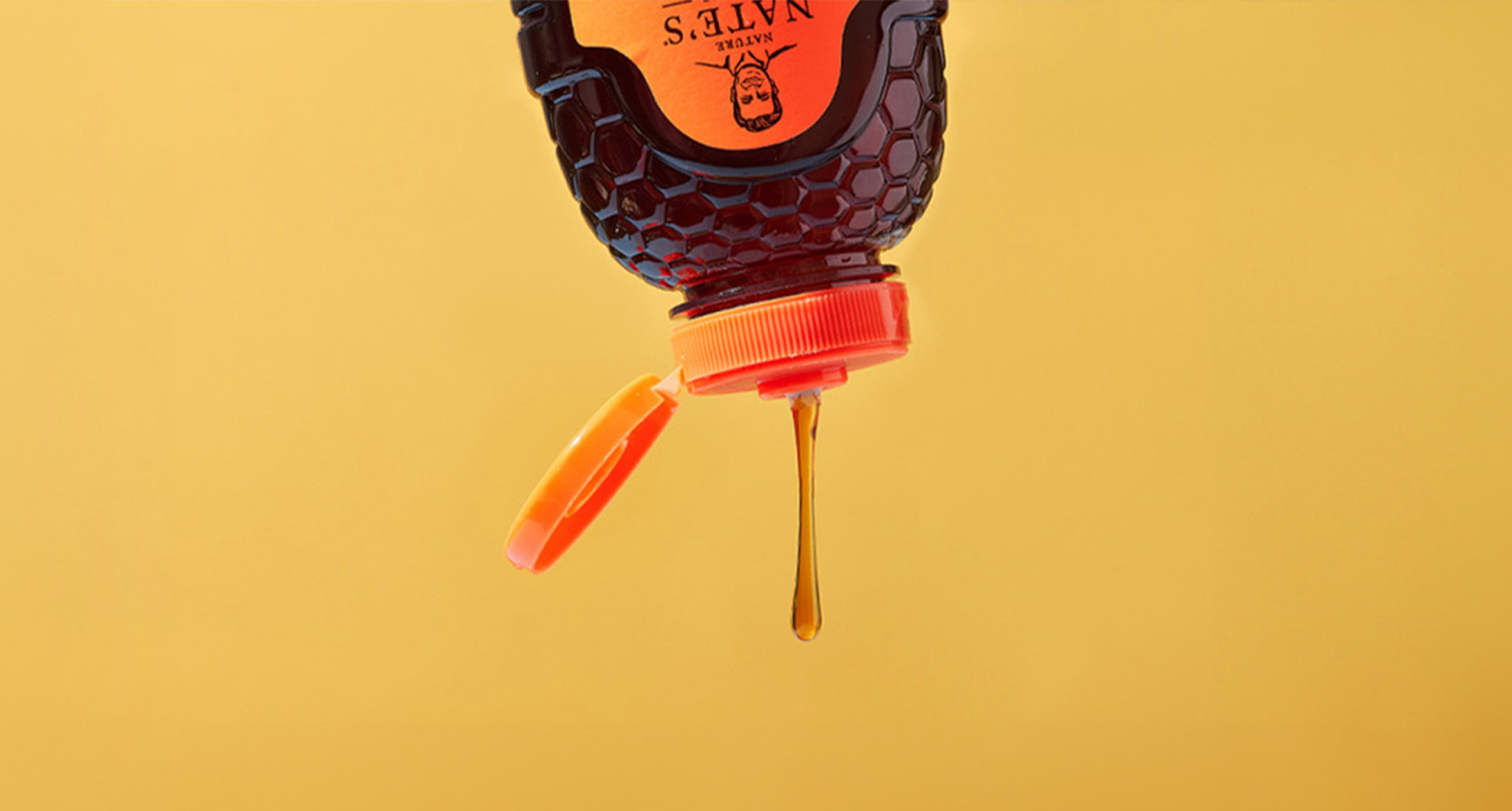 Nature Nate’s honey bottle upside down, honey dripping against a yellow background.