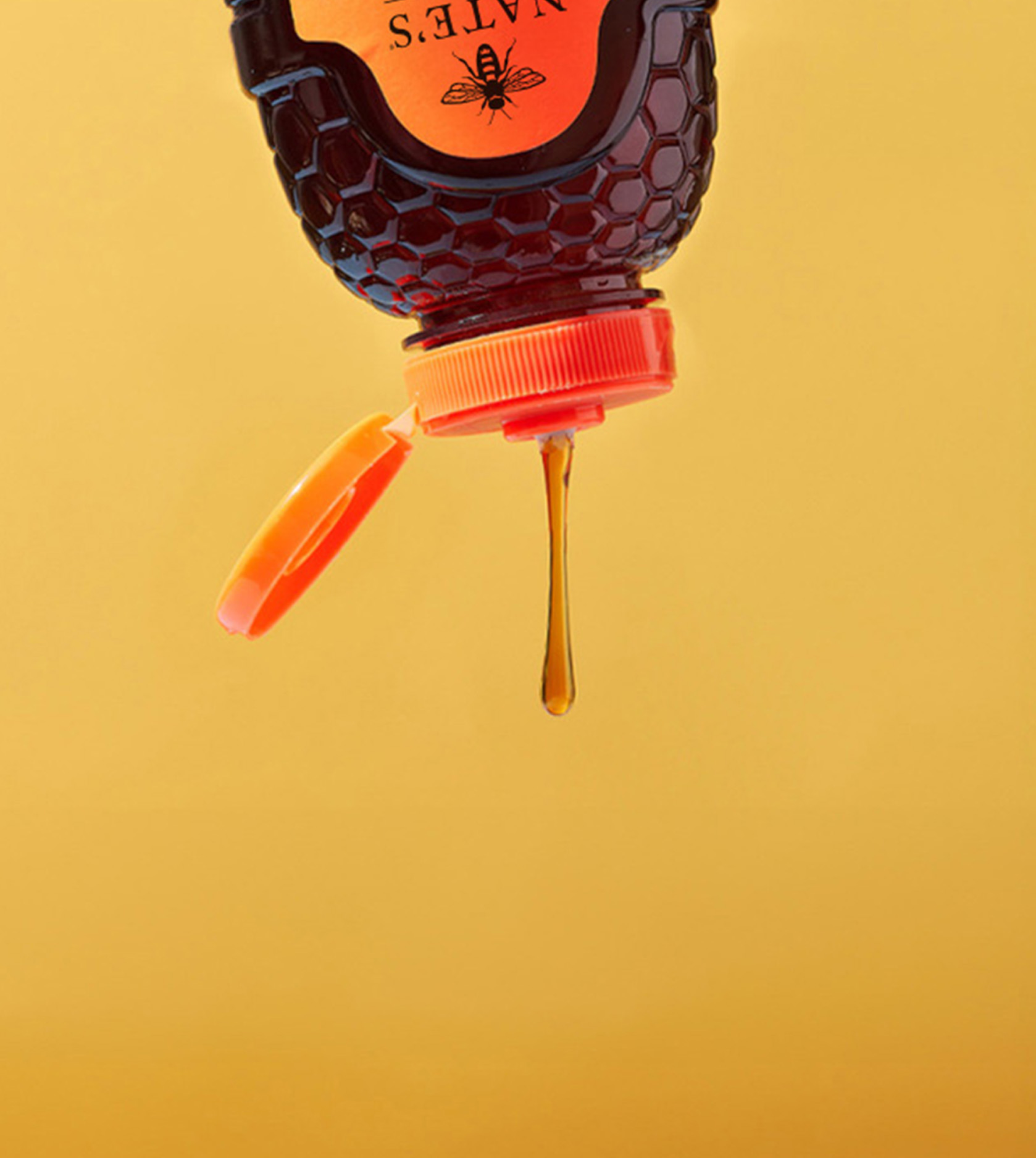 Nature Nate’s honey bottle upside down, honey dripping against a yellow background.