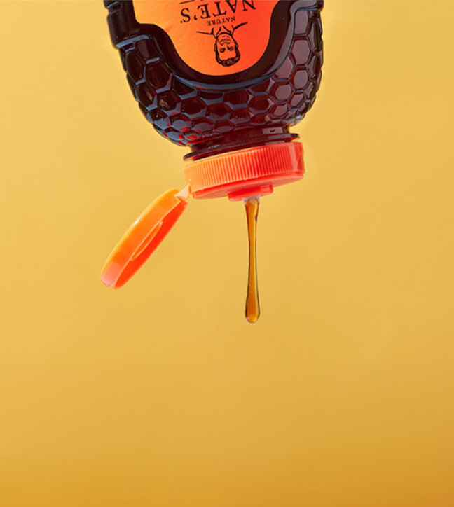 Nature Nate’s honey bottle upside down, honey dripping against a yellow background.