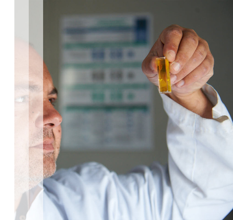 A scientist examines a vial with a golden substance.