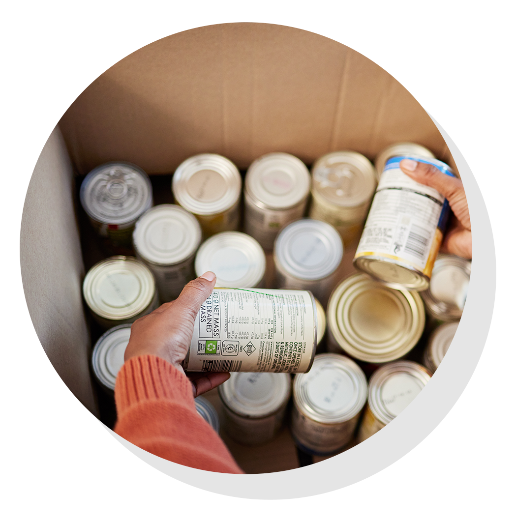 Person holding canned goods over a box filled with cans.