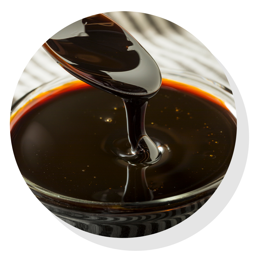 Thick, dark molasses pouring from a spoon into a glass bowl, against a striped background.