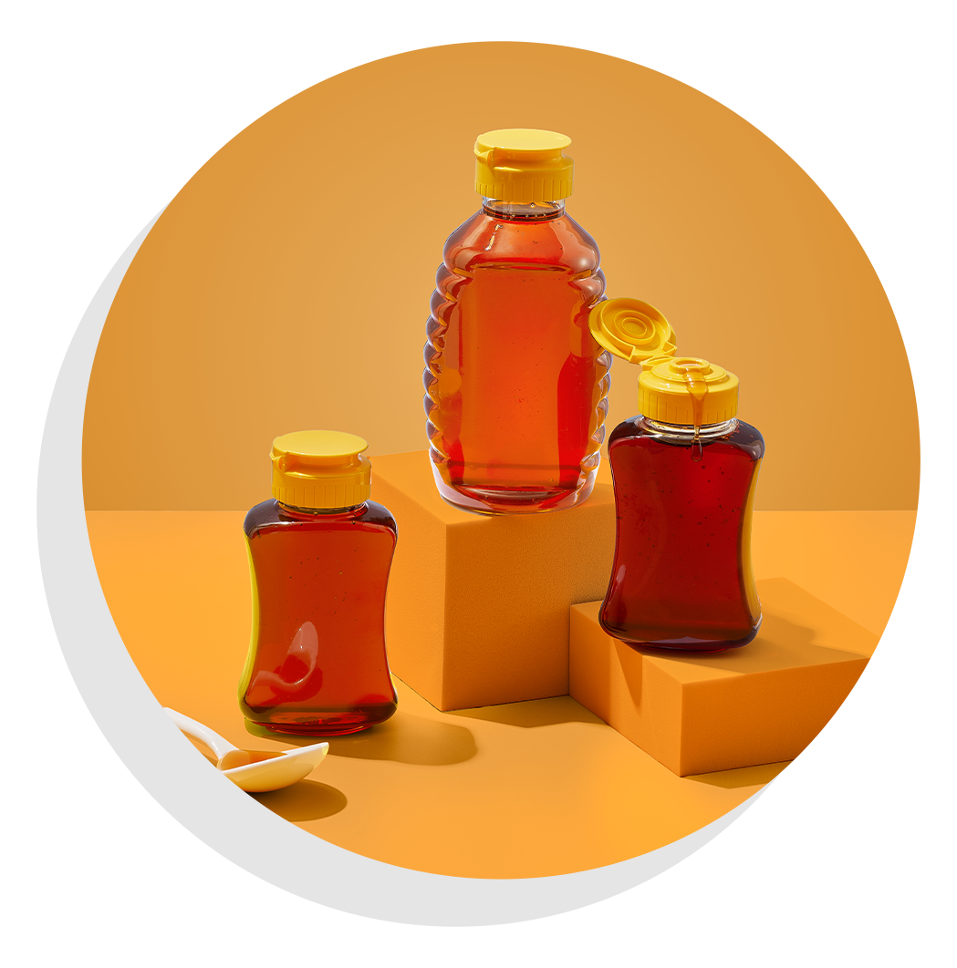 Three squeeze bottles filled with honey displayed on stacked blocks against a warm golden background.