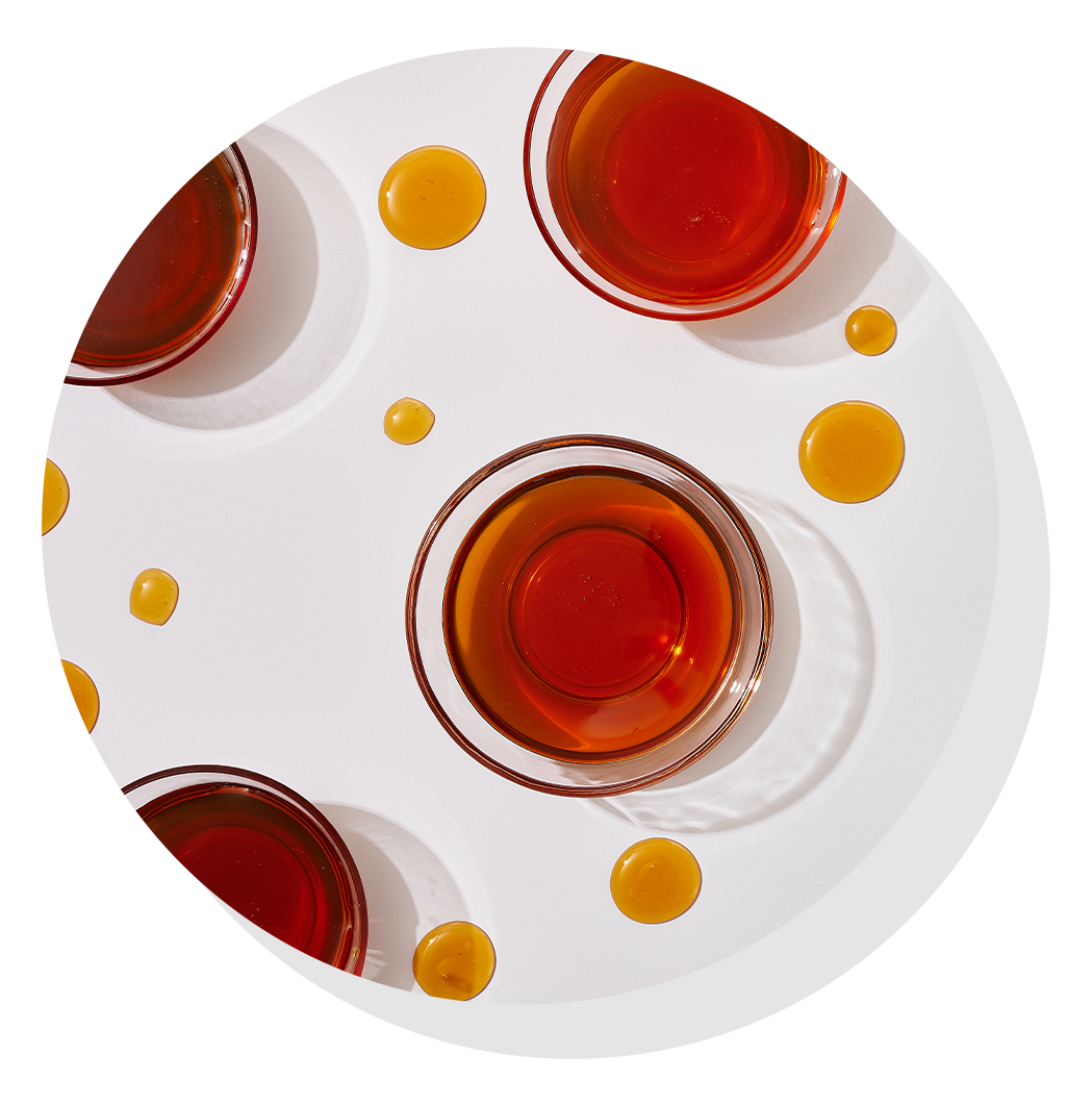 Top‑down view of glass bowls filled with honey arranged on a white surface, with small drops of honey placed between them.